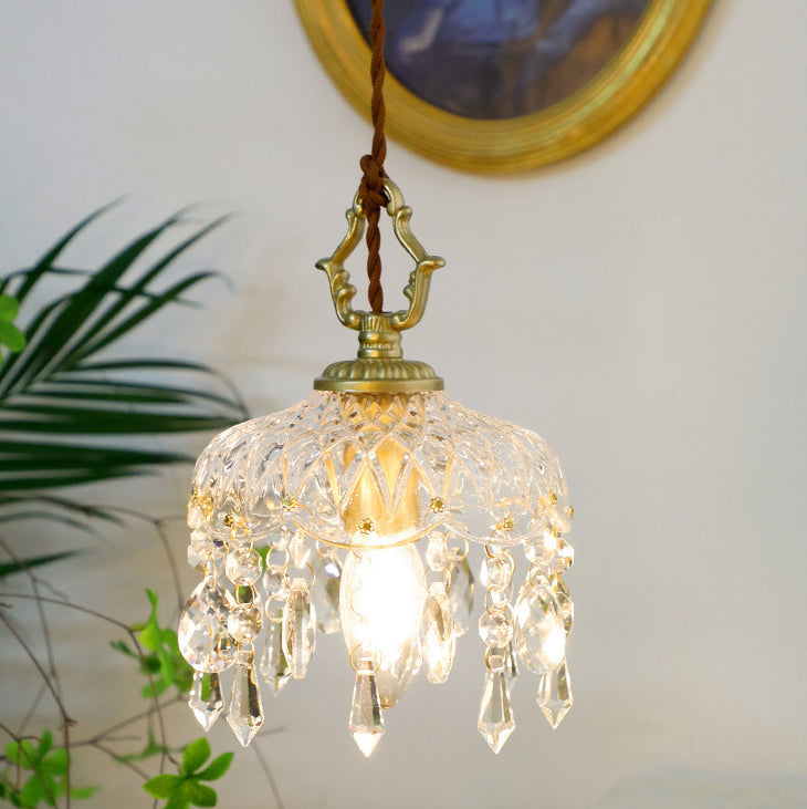 Lit glass pendant light with a gold cap near a leafy palm plant