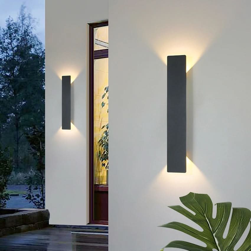 Two black up and down LED wall sconces beside a doorway on a light facade