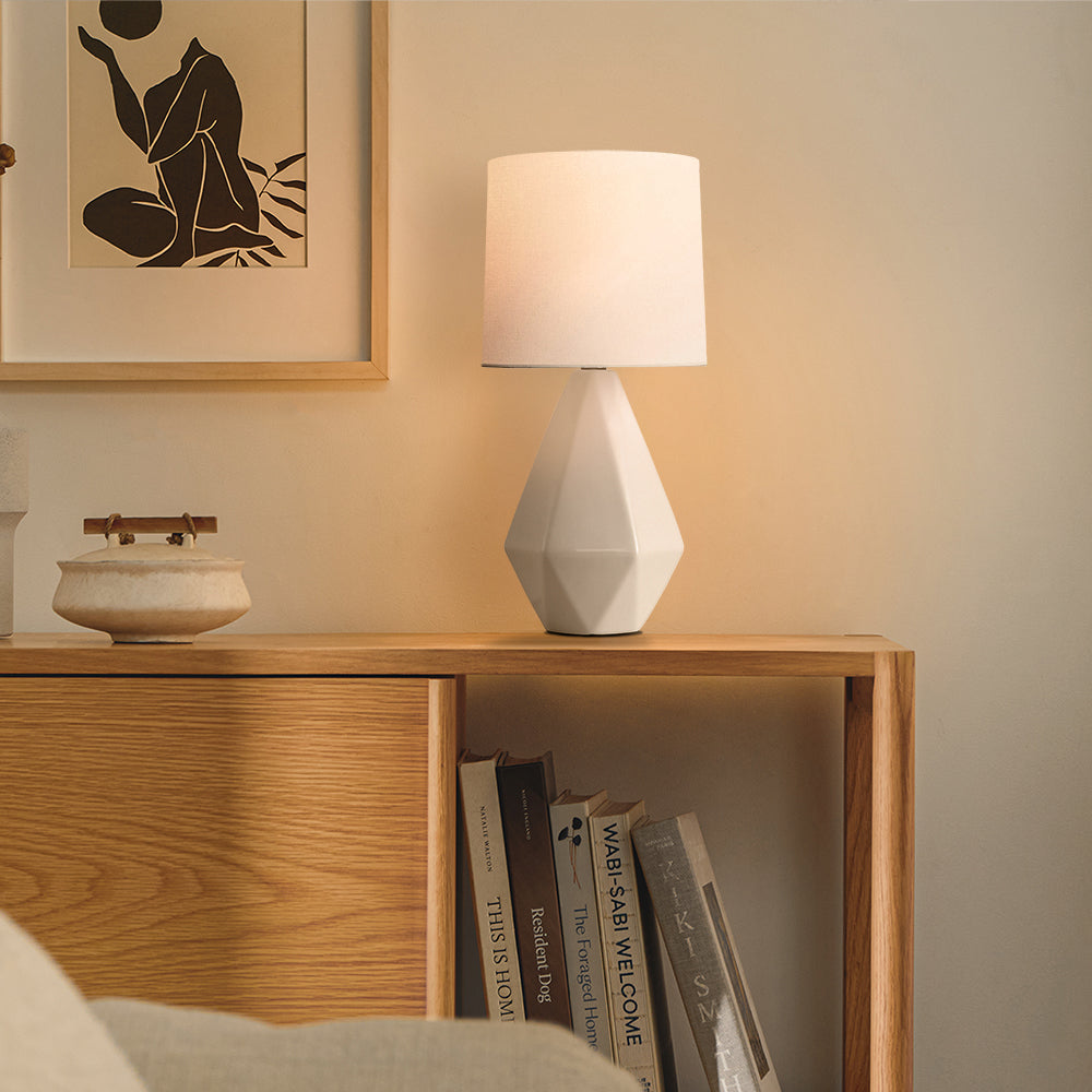 Lit white ceramic table lamp on an oak console with books below