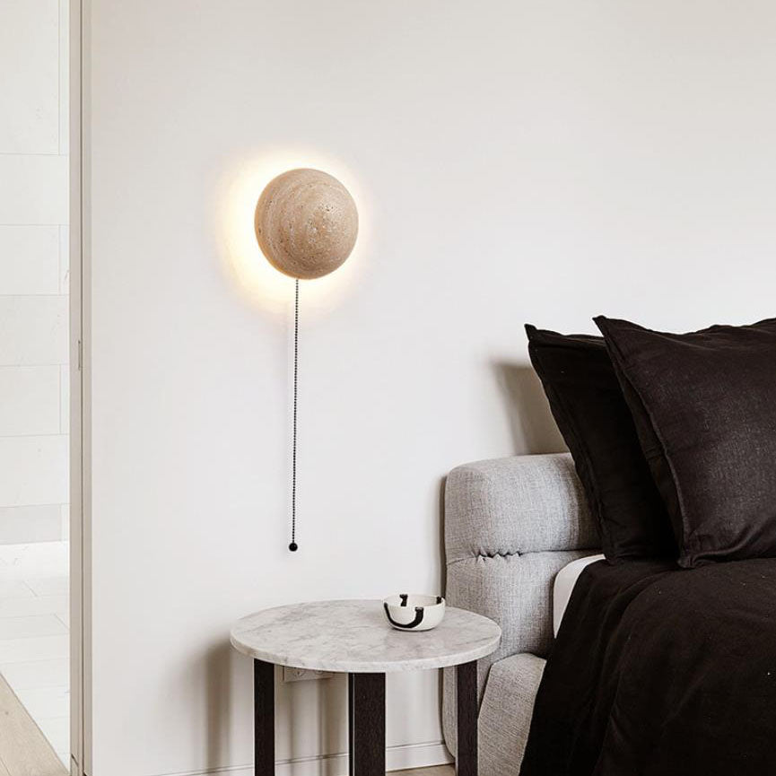 Stone LED sconce with a pull-chain above a marble bedside table in a bedroom