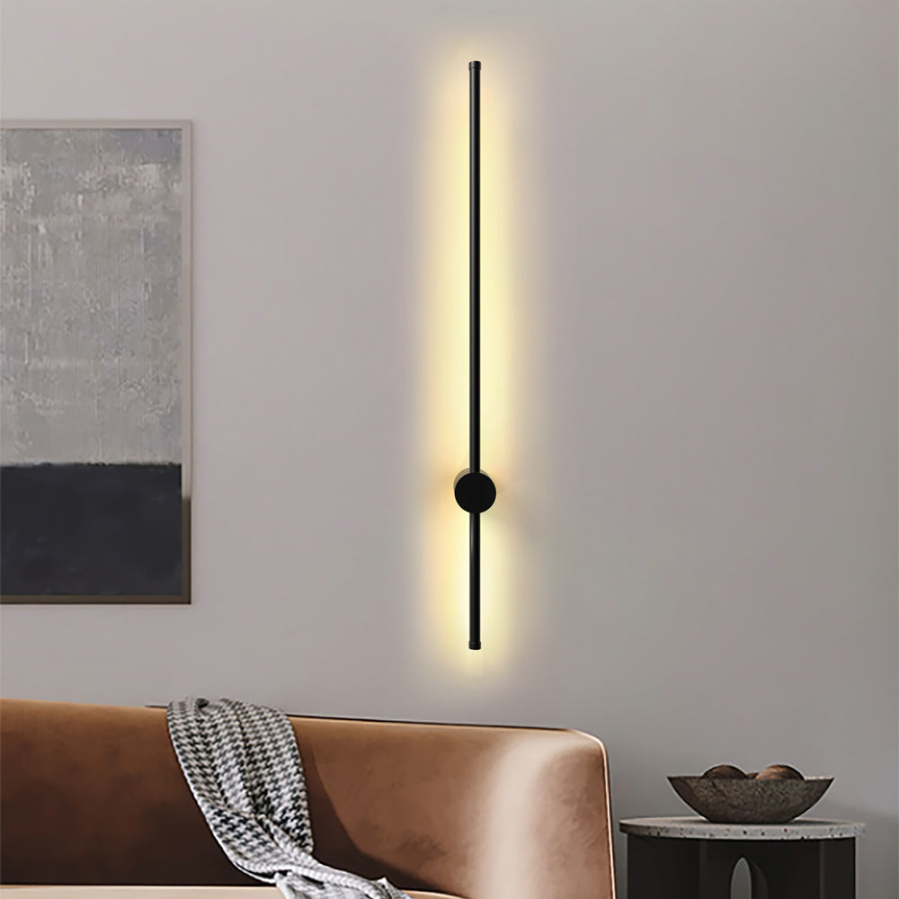 Single vertical black linear wall light above a tan leather sofa