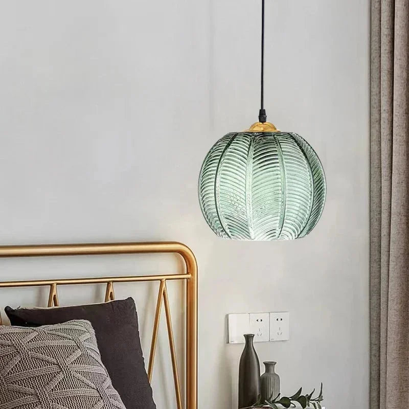 Warm glowing palm leaf glass pendant lighting a bedside corner at night