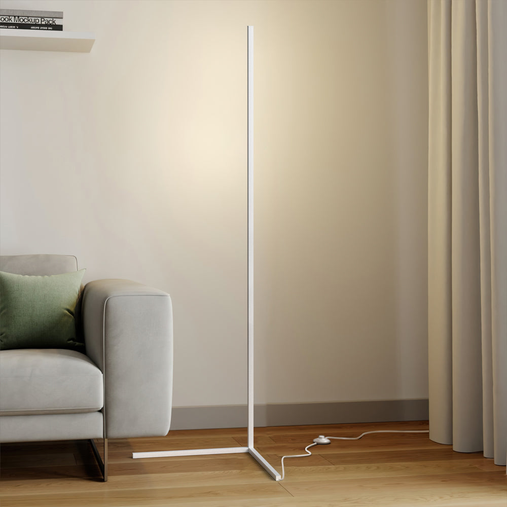 White floor lamp on a triangle base with foot switch cord near a grey sofa