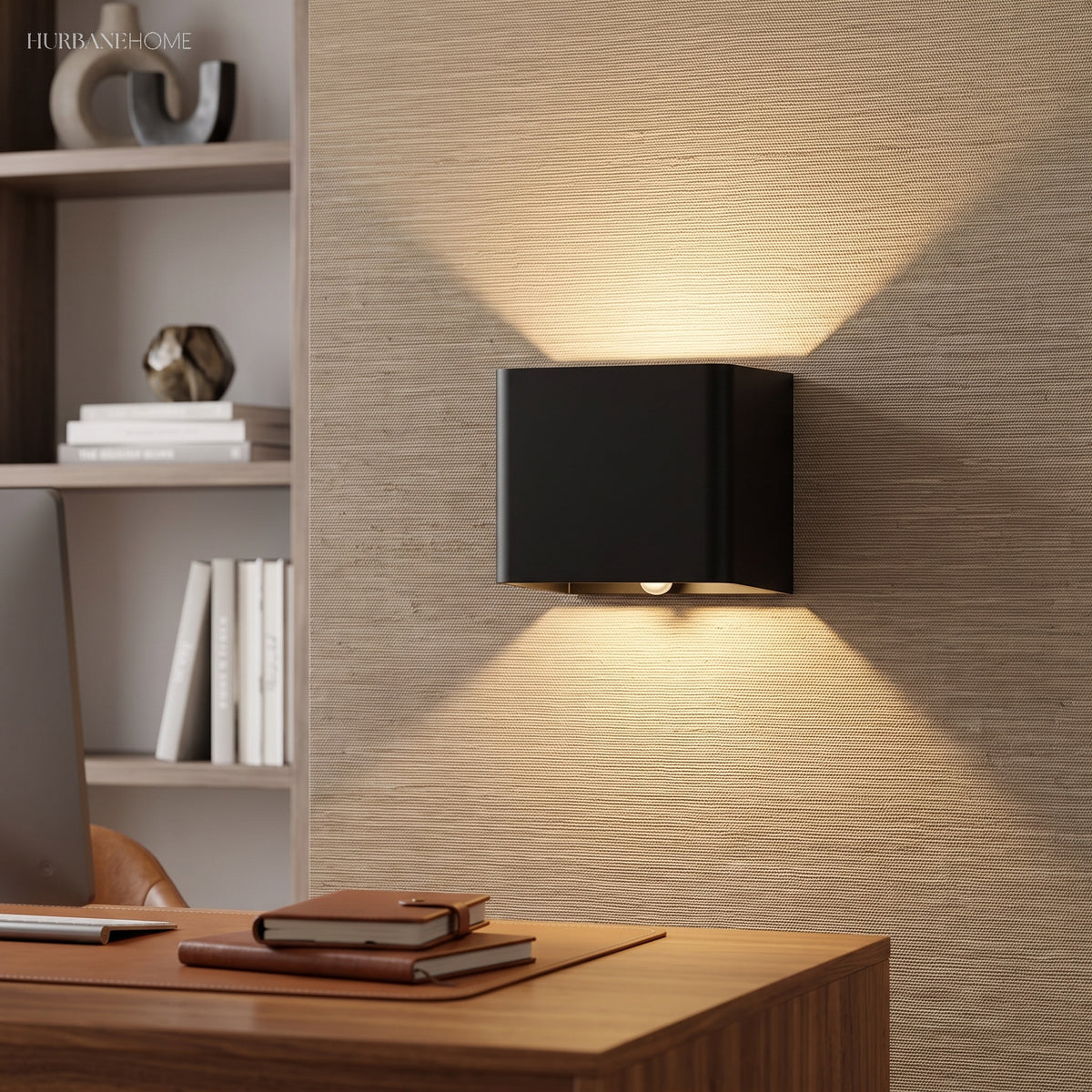 Black cube wall sconce lit on a textured wall above a desk