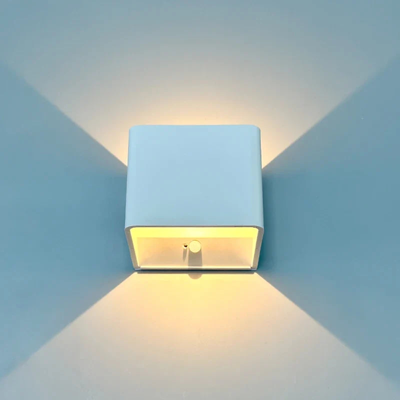 White cube wall sconce lit on a blue wall showing both beams