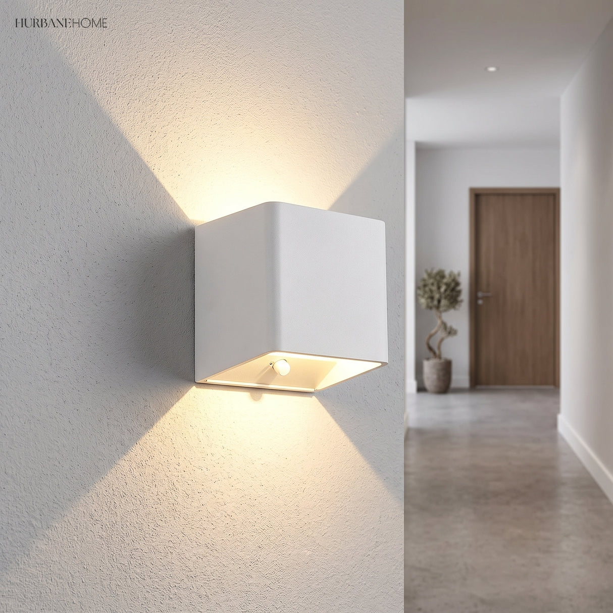 White cube wall sconce lit on a wall beside a hallway doorway
