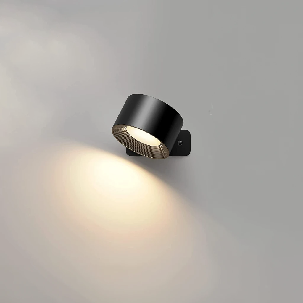 Black puck light angled to wash a plain wall with warm light
