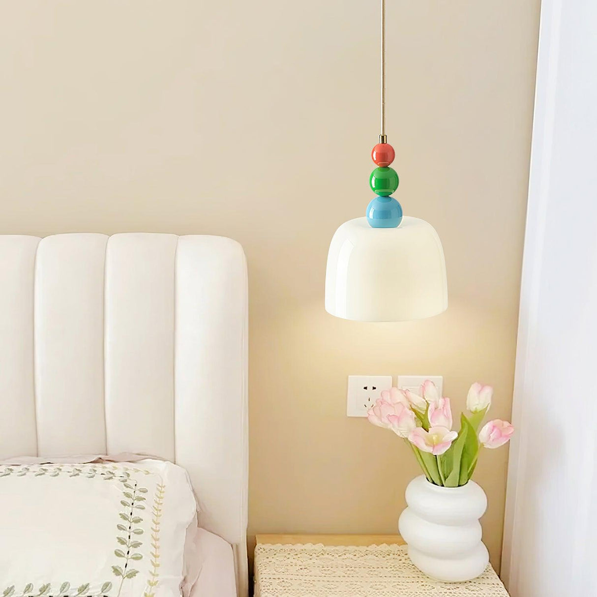 Beaded pendant lit beside a padded headboard and a vase of pink tulips