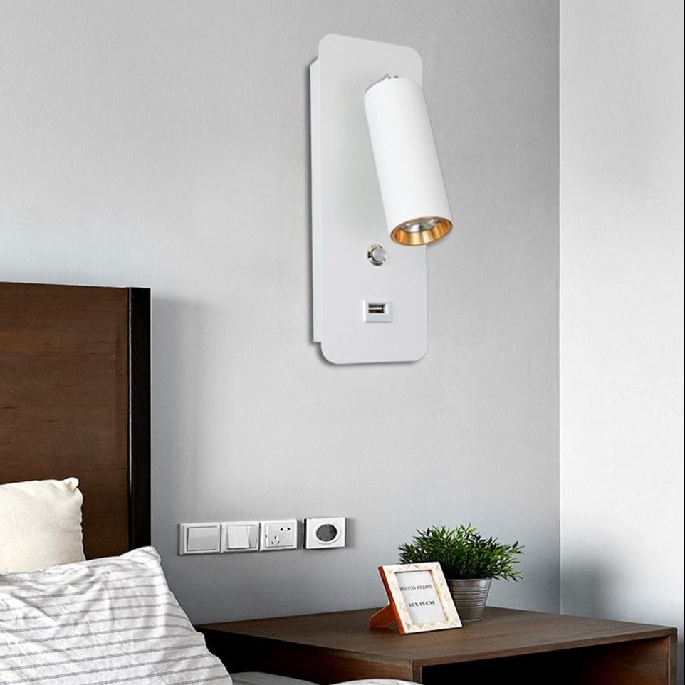 White bedside reading light lit above a bed with a framed photo