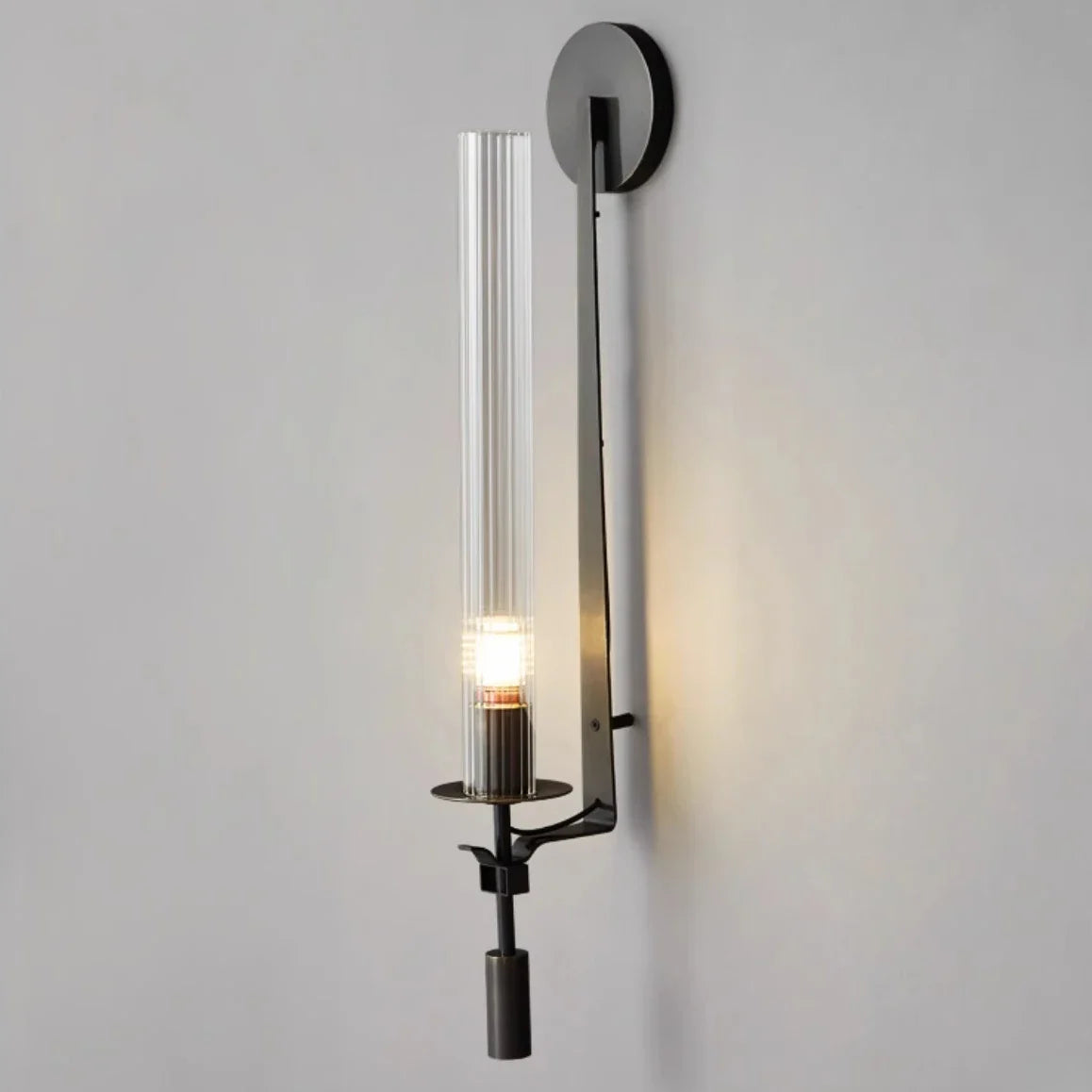 Black fluted glass sconce with an exposed candle bulb lit warm