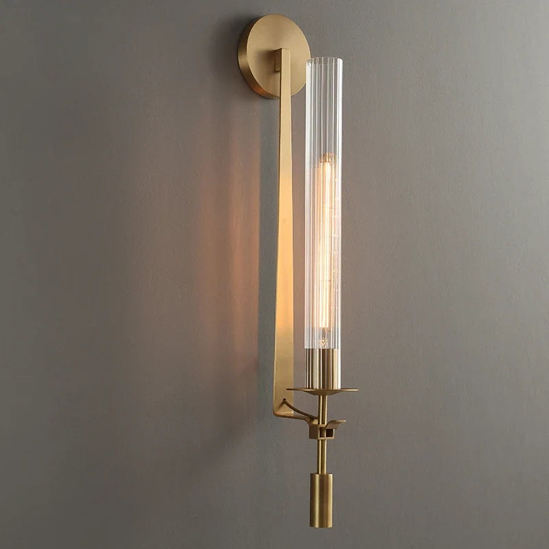 Gold fluted glass sconce lit on a grey wall seen at an angle