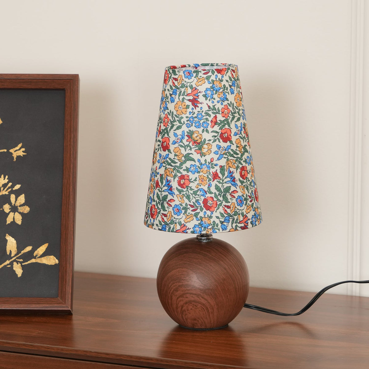 Blue ground floral shade lamp lit on a sideboard with the cord visible