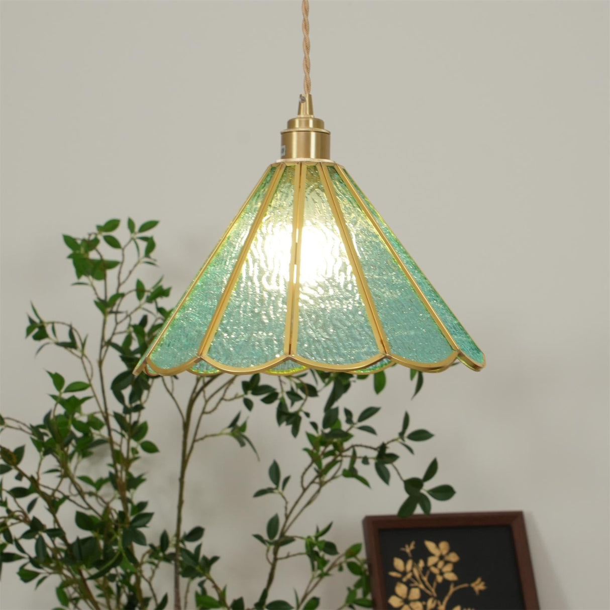 Blue glass pendant seen through green branches with the panels lit