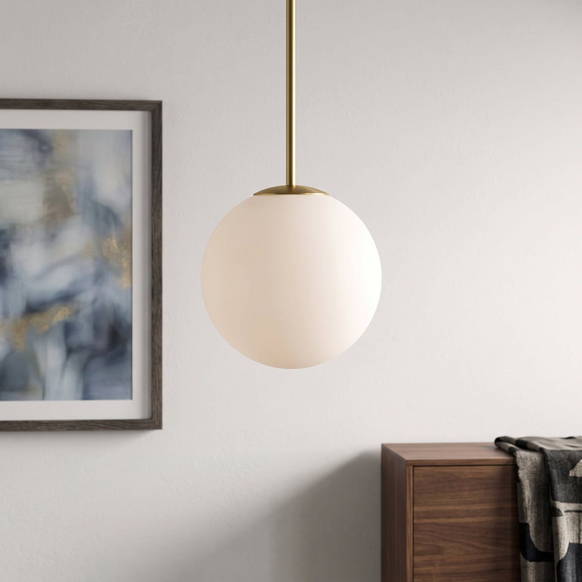 Opal glass globe pendant on slim brass stem beside framed artwork