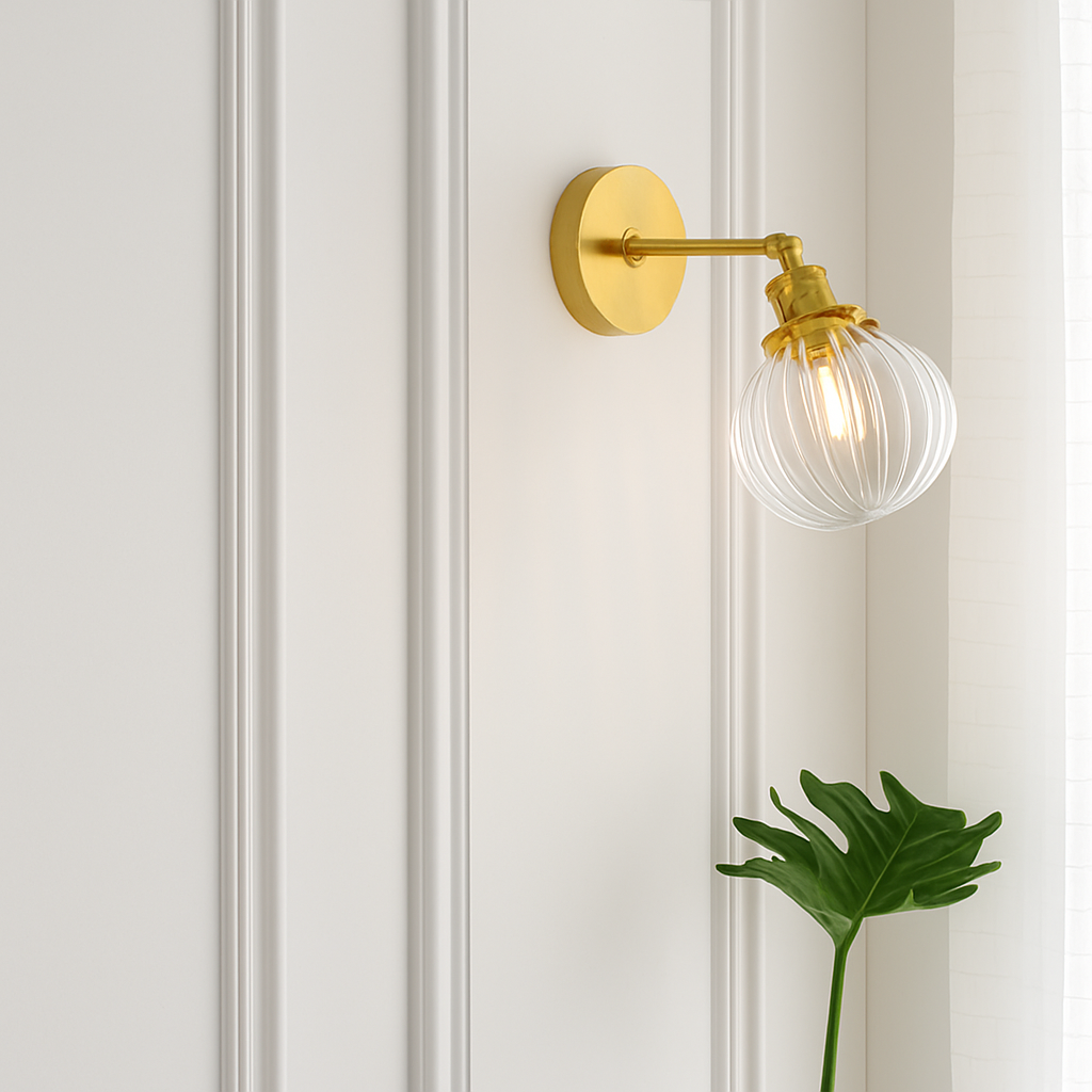 Brass sconce with clear ribbed glass on a white paneled wall by a plant