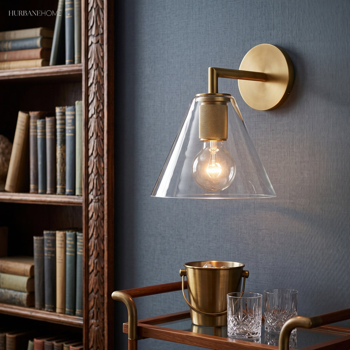 Cone shade sconce lit warm beside a bookcase and a brass bar cart