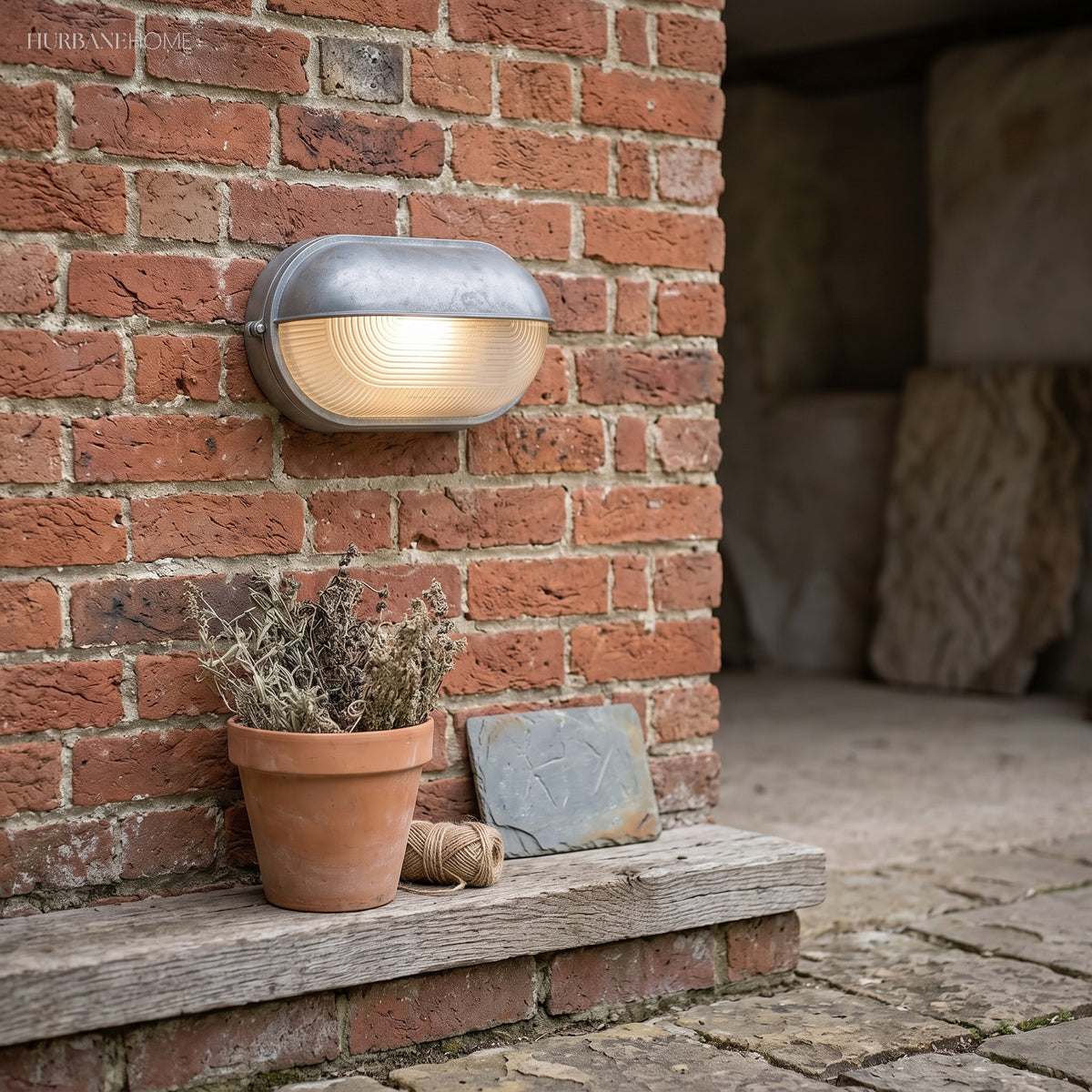 Silver bulkhead lamp on a red brick wall above a terracotta pot and step