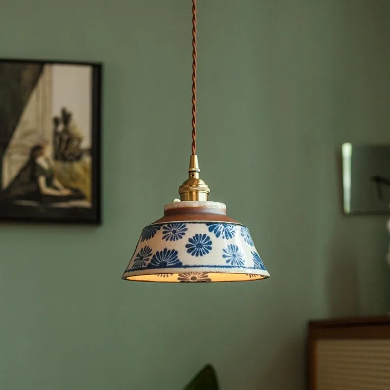 Blue daisy ceramic pendant lit against a deep green wall