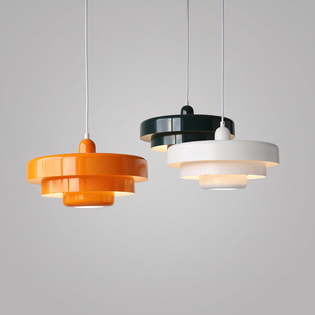 Three tiered pendant lights in orange, dark green and white hanging together