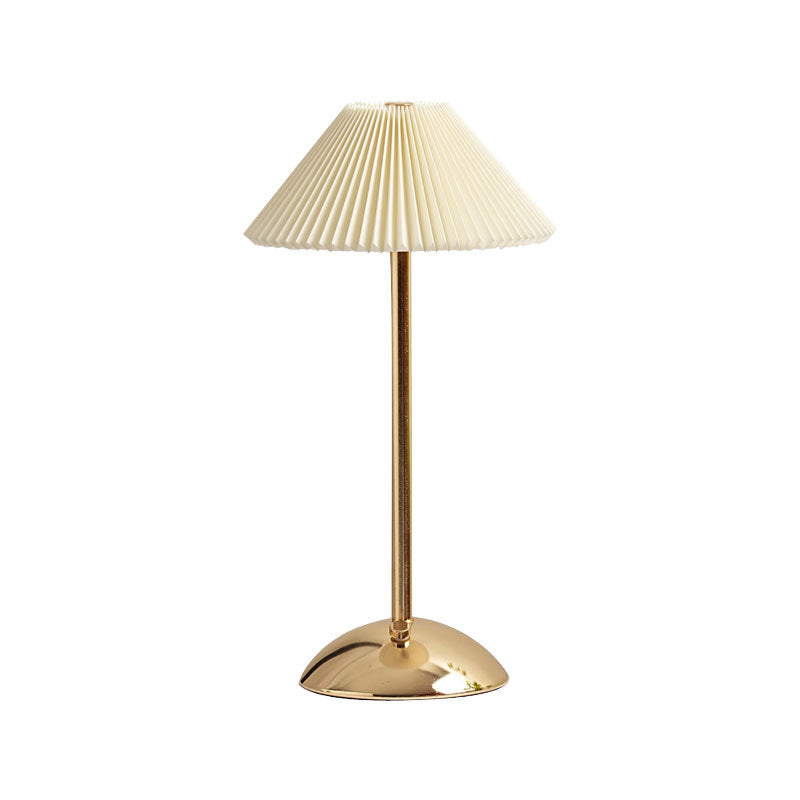 Gold pleated table lamp viewed from the side on a plain backdrop