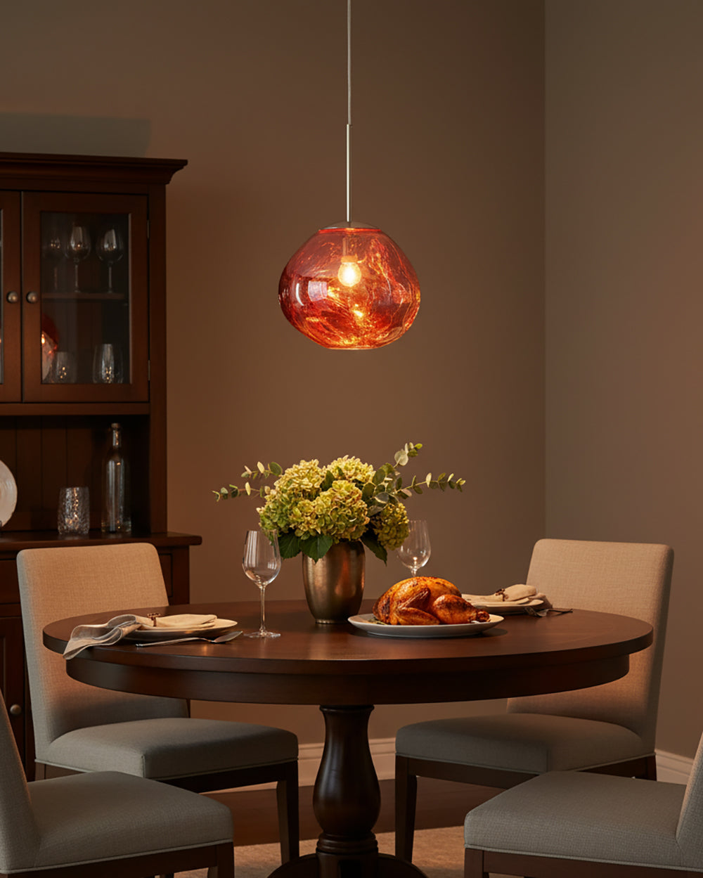 Copper pendant lit above a round dining table beside a dark glazed cabinet
