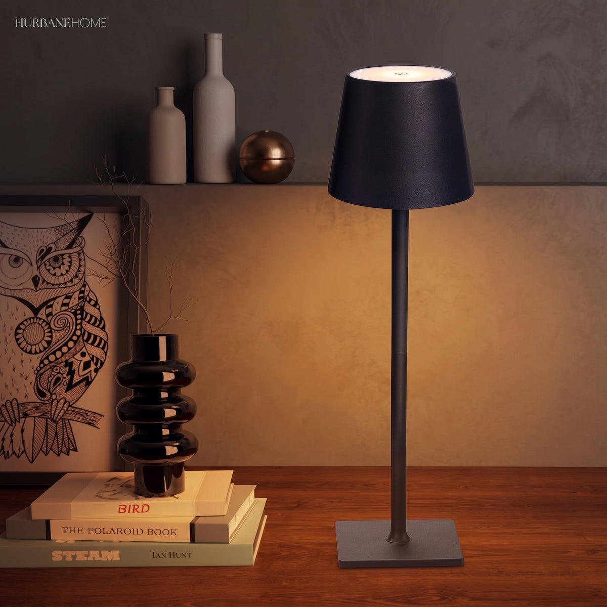 Black cordless lamp glowing beside stacked books and ceramic vases