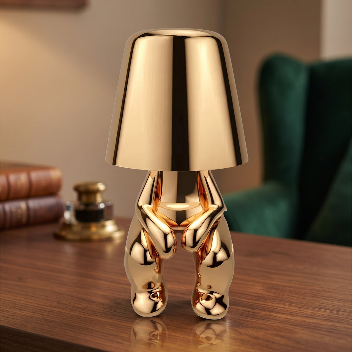 Gold figurine table lamp lit on a walnut desk beside books