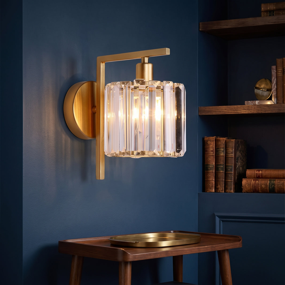 Gold sconce with a clear crystal column shade on a navy wall