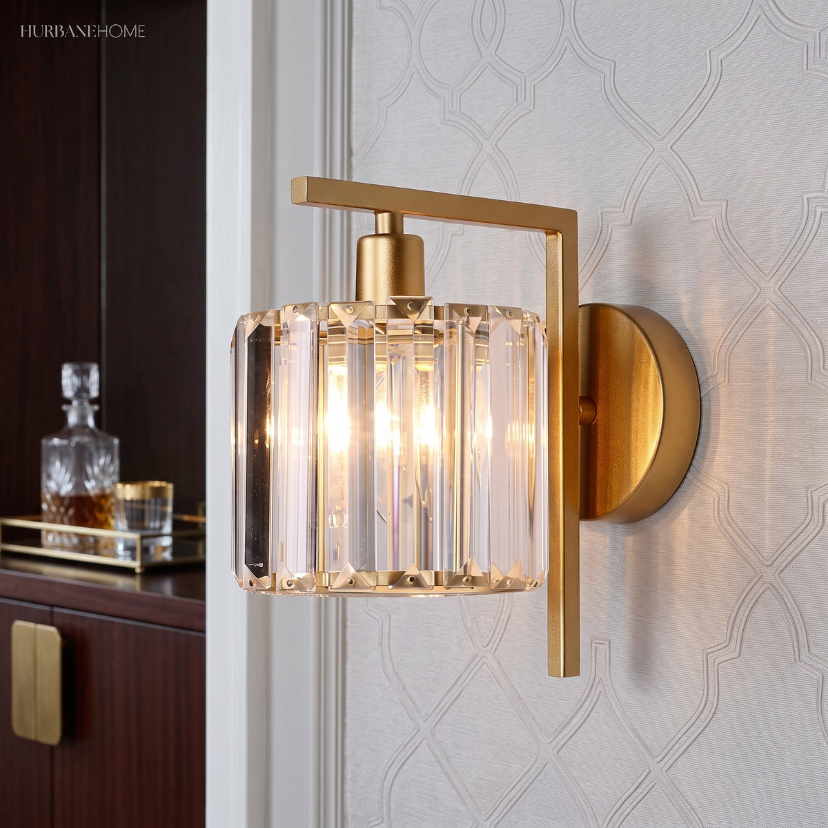 Crystal column sconce lit on a patterned wall beside a decanter