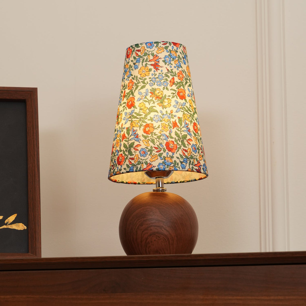 Floral table lamp lit low, showing the bulb glow through the fabric shade