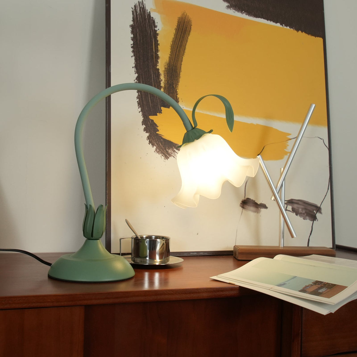 Drooping petal shade lit on the curved stem in front of framed artwork