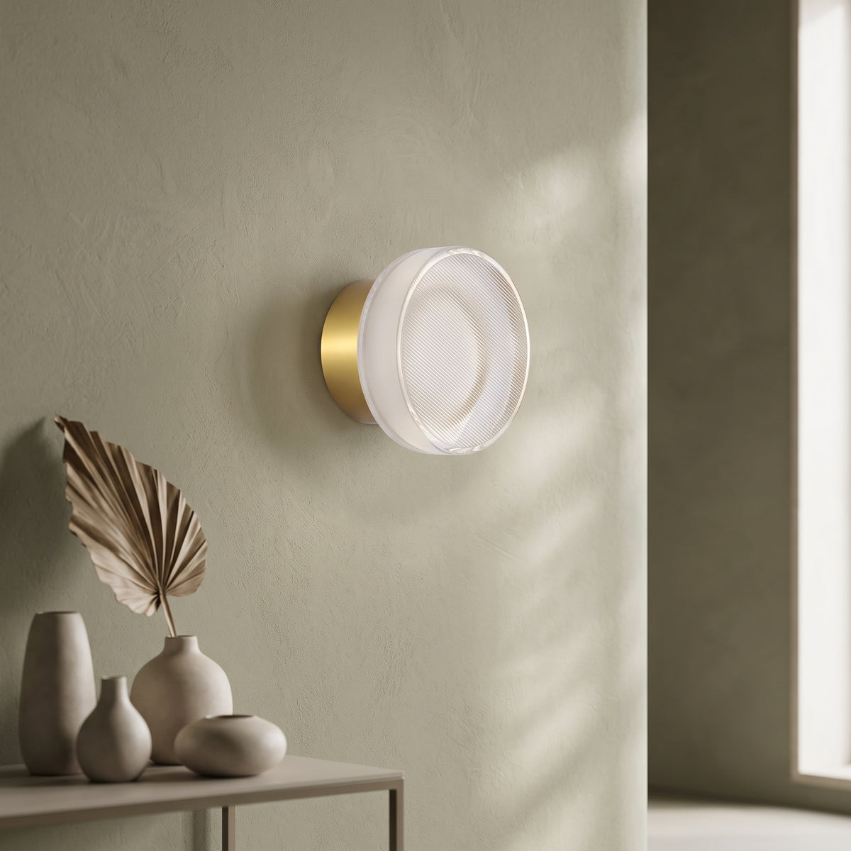 Gold ribbed acrylic wall light lit on an olive wall above vases