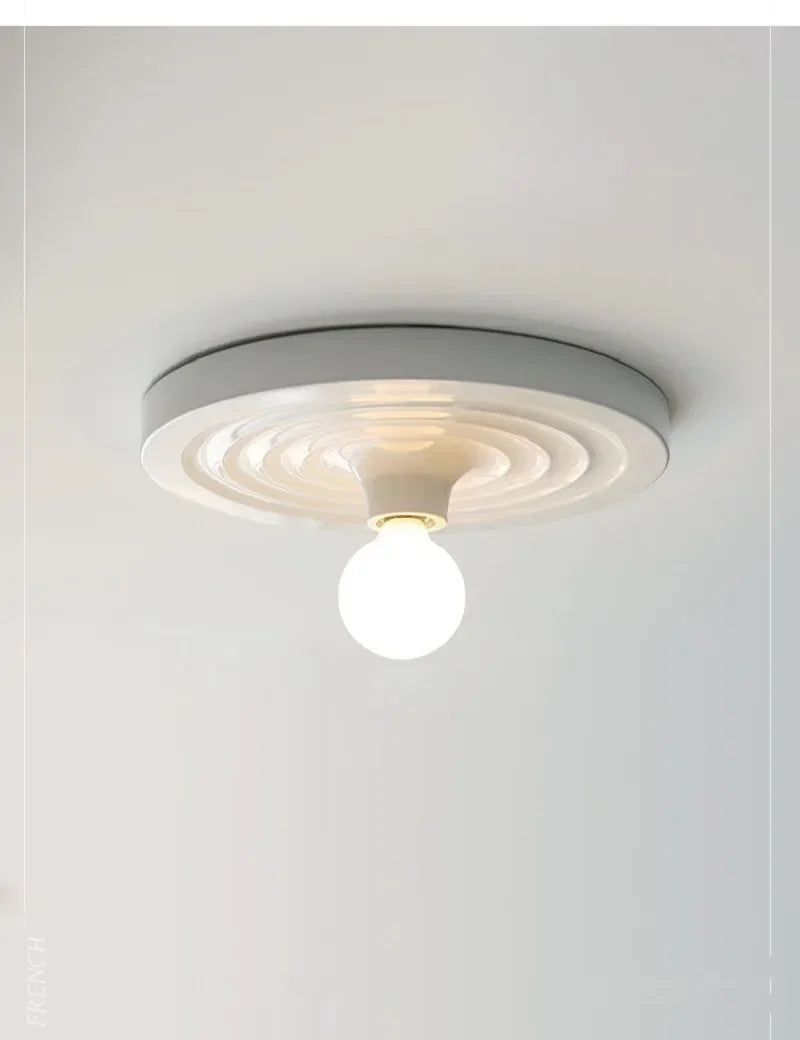 White disc ceiling light with a round opal bulb below it