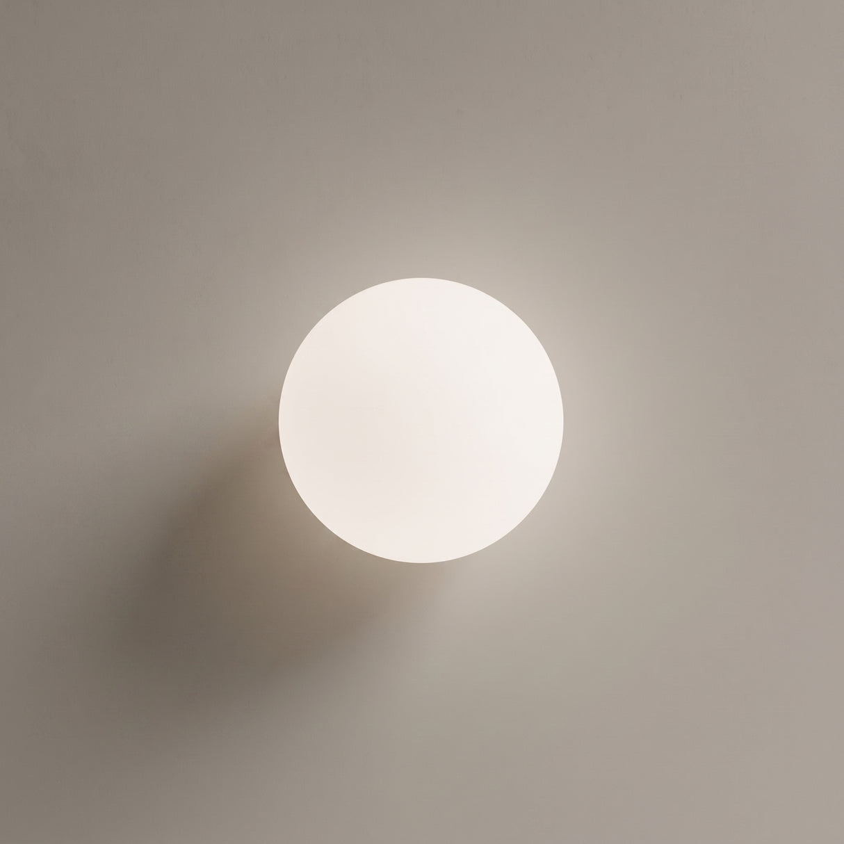 White glass globe ceiling light with gold base on a plain wall
