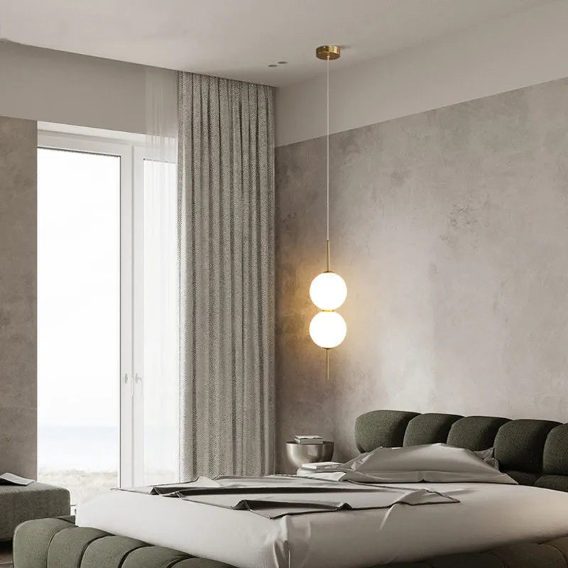 Single globe pendant lit in a pale bedroom beside a balcony door