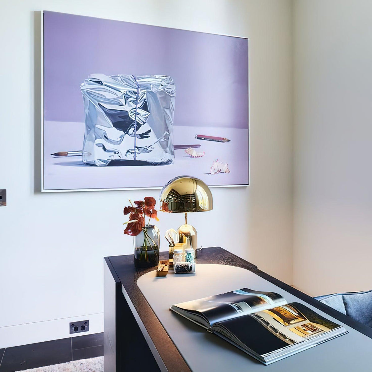 Gold dome lamp lit on a desk in front of a large framed artwork