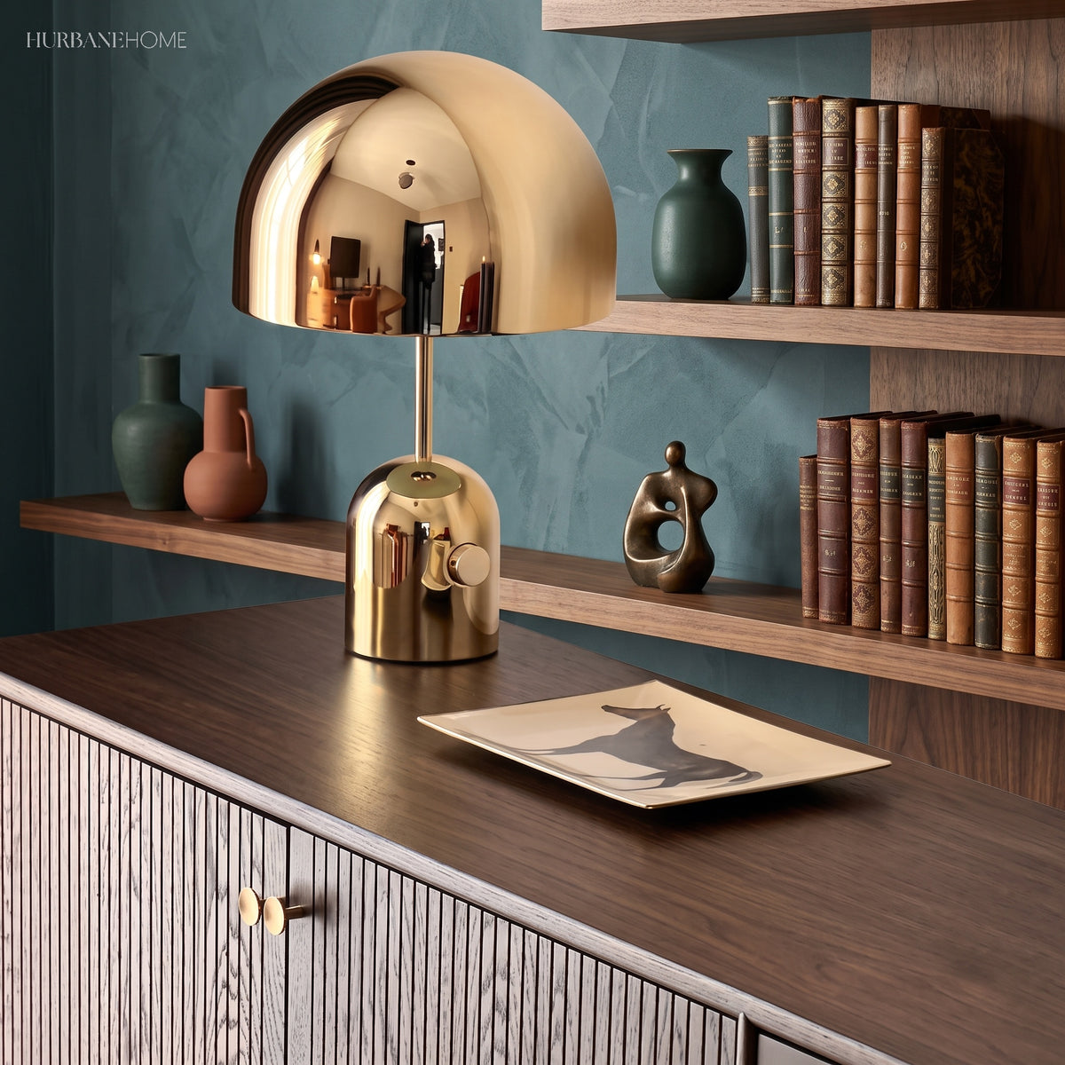 Gold dome table lamp on a fluted sideboard against a teal shelved wall