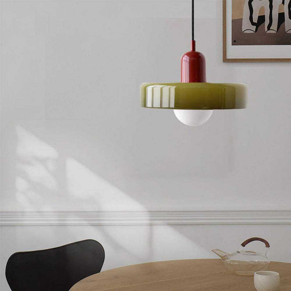 Green glass pendant light with a red lamp holder above a round oak dining table