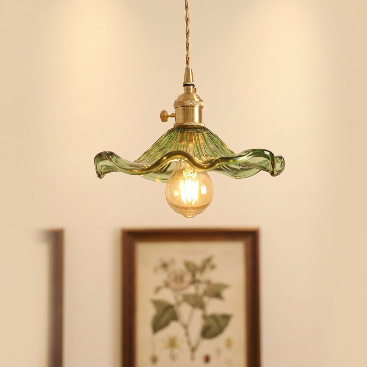Green hibiscus glass pendant with a brass holder above a framed botanical print