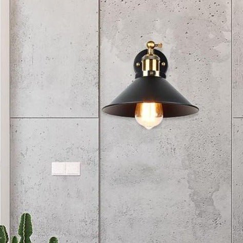 Black cone shade wall sconce lit against a concrete panelled wall