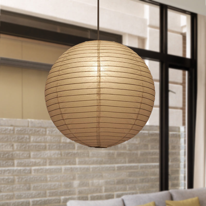 Round globe paper lantern lit in front of a pale brick wall