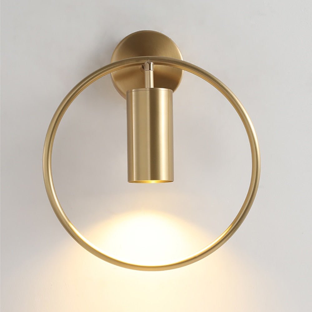 Brass ring wall sconce lit against a plain pale wall