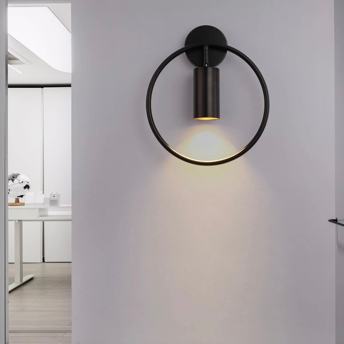 Black ring wall sconce lit on a white wall in a doorway