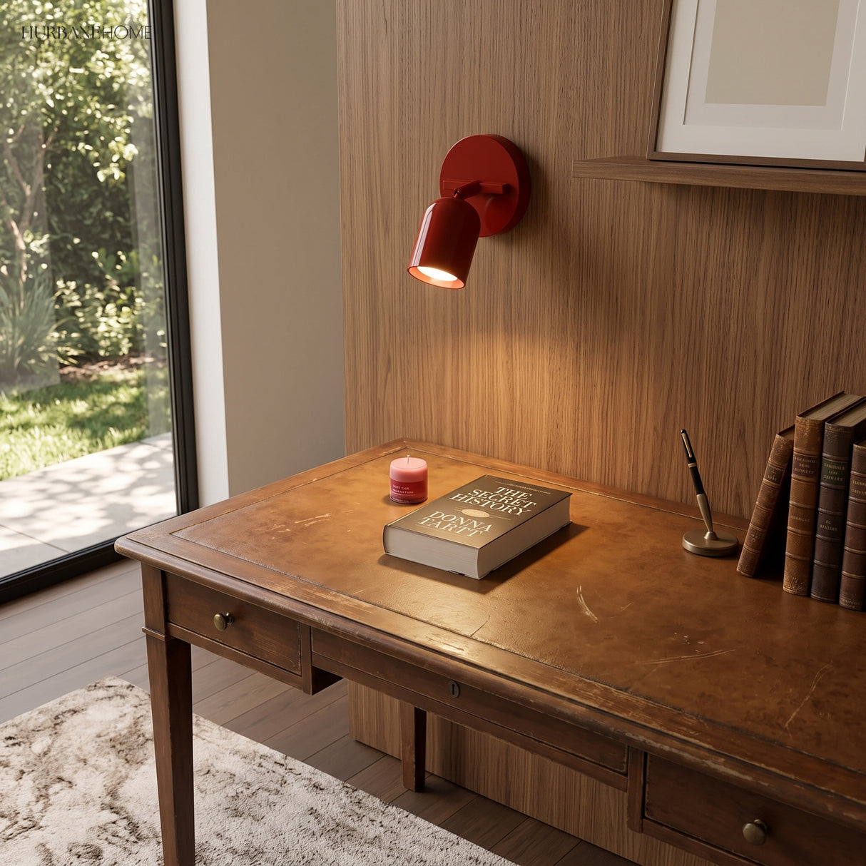 Red adjustable wall sconce mounted above a leather-top writing desk with books