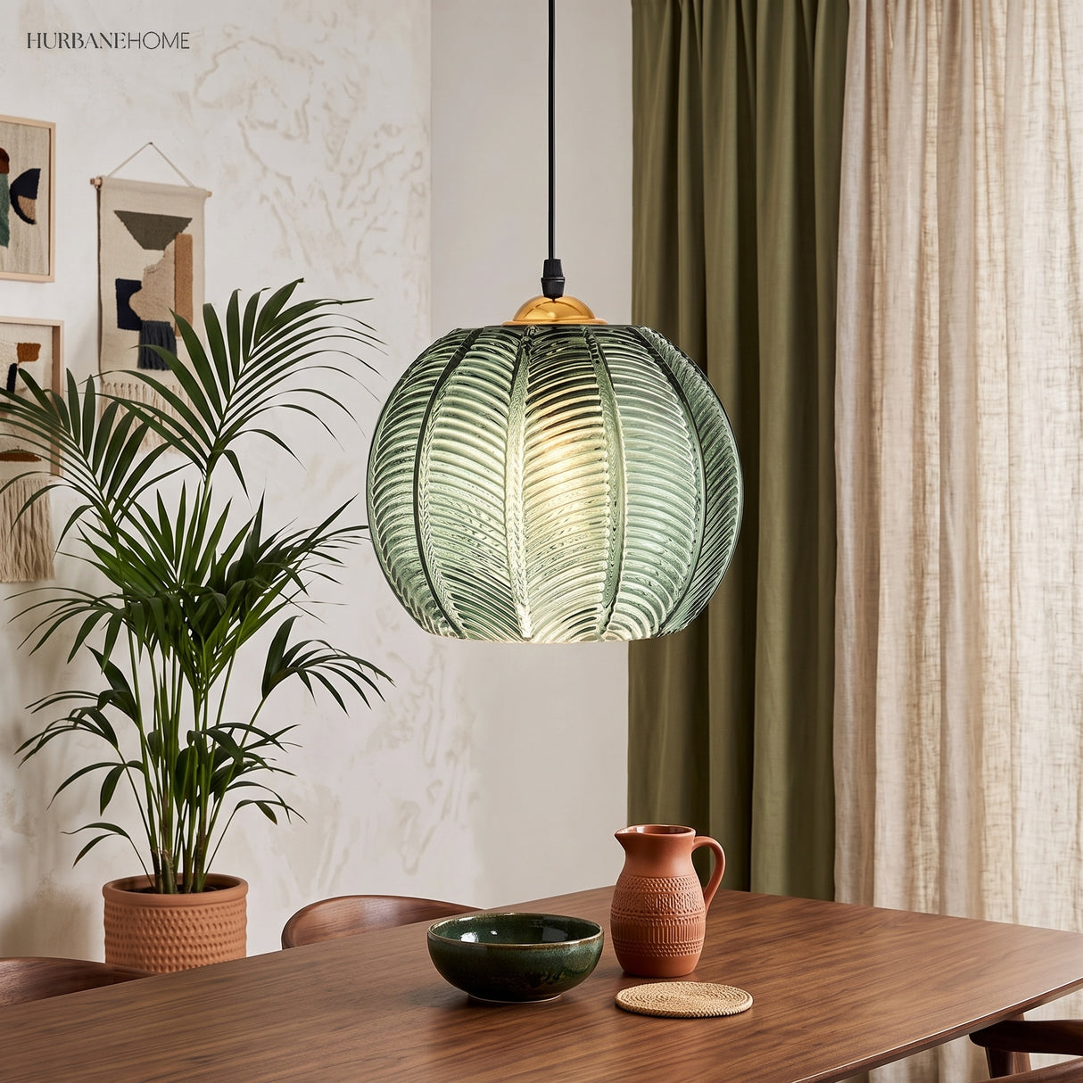 Glowing palm leaf glass pendant next to a tall potted palm and framed boho wall art