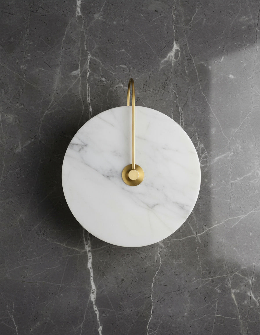 Unlit marble disc on a gold arm against grey veined stone