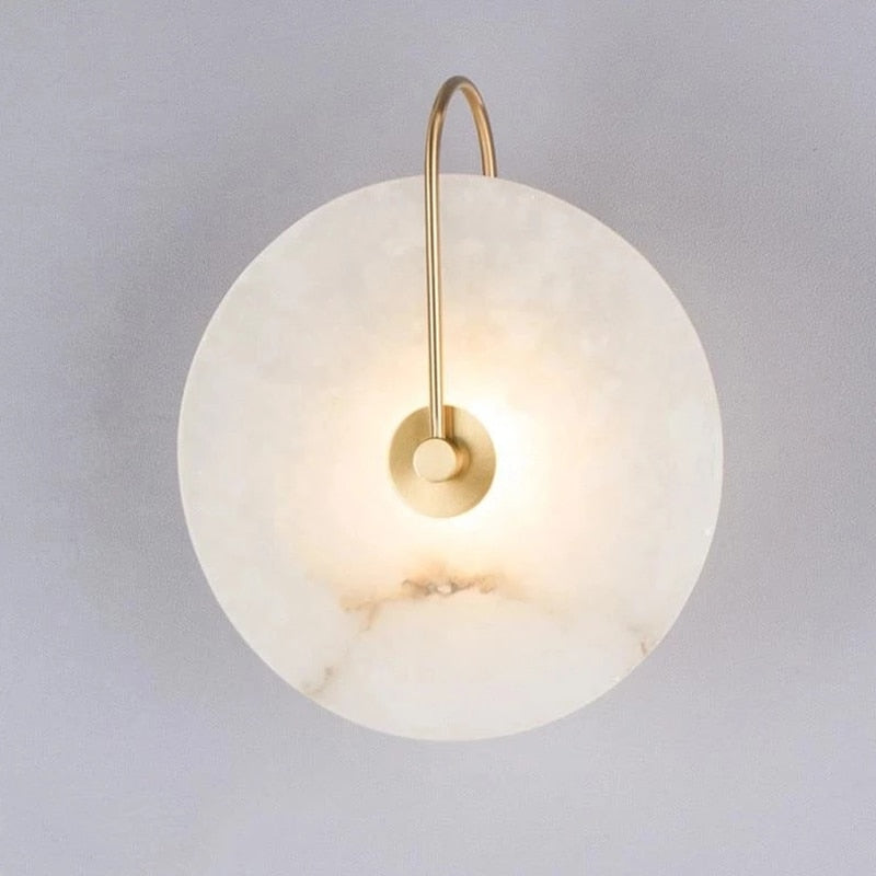 Marble disc sconce on a gold curved arm against a pale wall