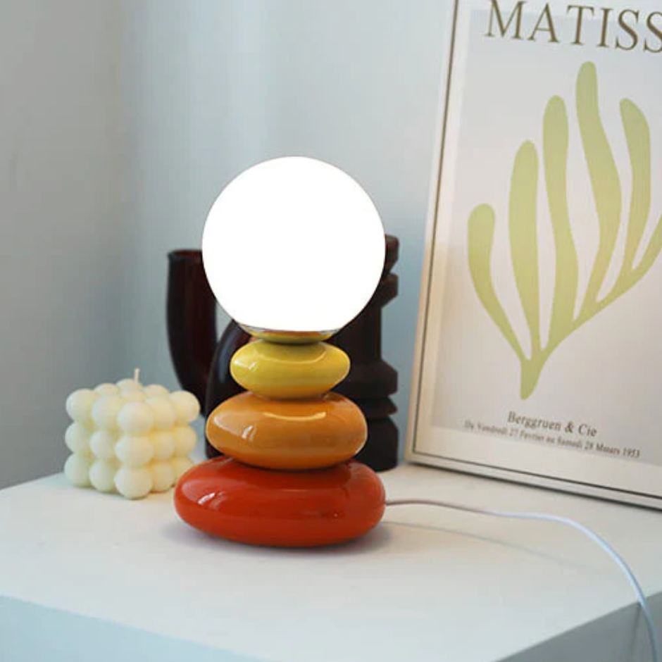 Orange and yellow stacked lamp lit beside a framed leaf print