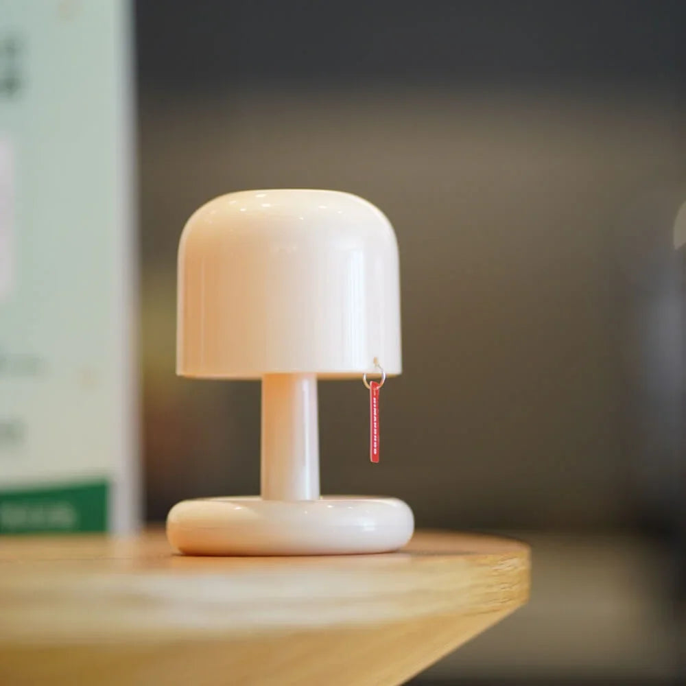 Cream mushroom shaped cordless table lamp with a red pull tag on timber