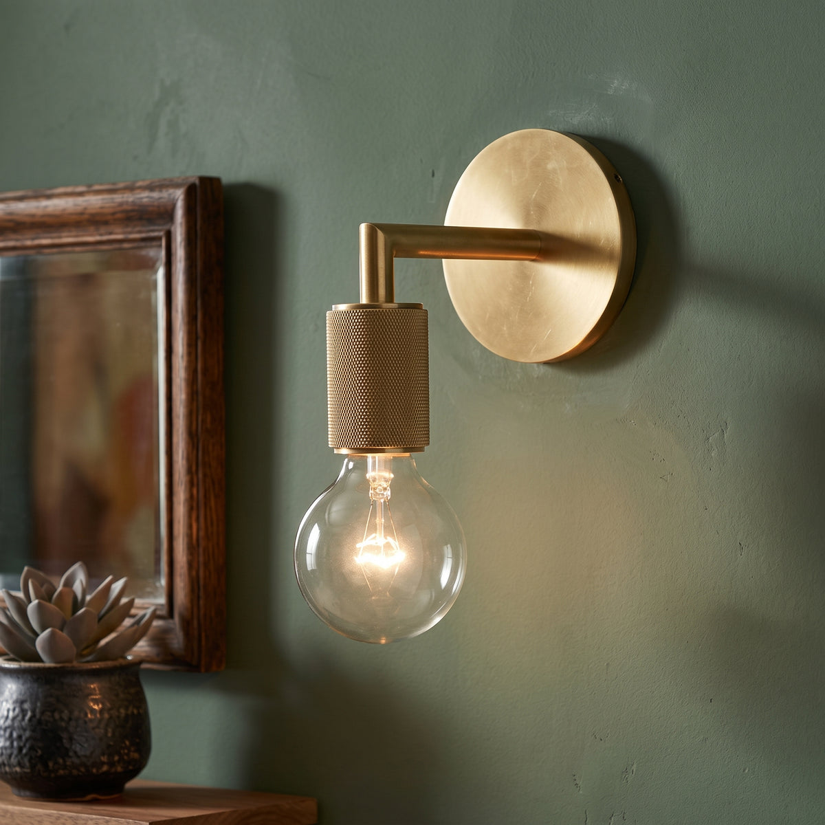 Brass wall sconce with a bare globe bulb on a sage green wall